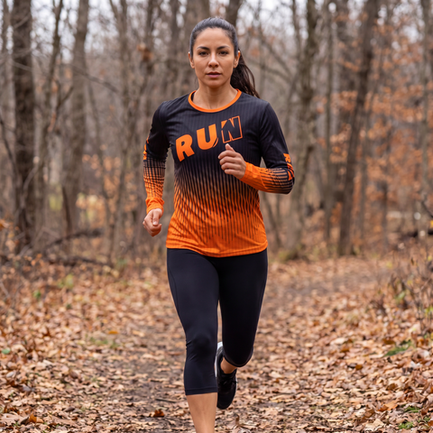 Female athlete running outdoors in a black and orange RUN REST LIFT REPEAT long sleeve performance shirt