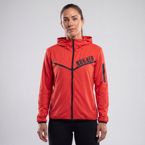 A woman wearing an orange hooded Runner Jacket with a full-zip front and black accent details, standing against a light gray studio background.