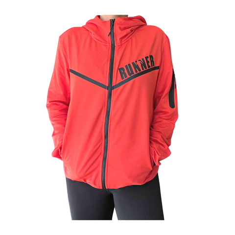 Woman wearing an orange Runner Jacket with a full-length zipper, attached hood, black chest graphics, and a zippered sleeve pocket, shown from the front against a light gray background.